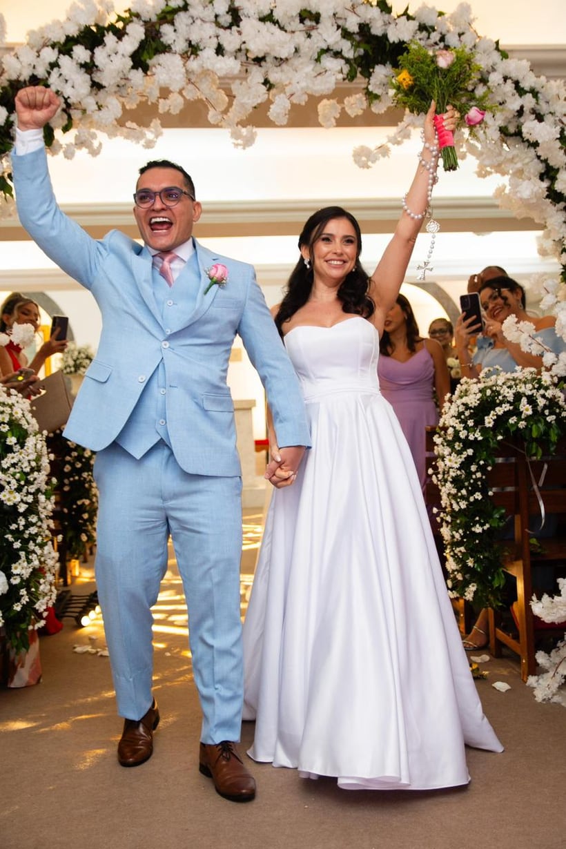 Noivos celebrando de mãos dadas sob um arco de flores, em cerimônia organizada pela LP Assessoria e Cerimonial
